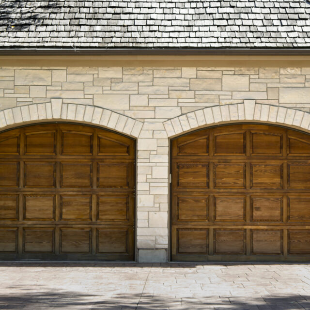 Double wooden garage doors in a white brick house.